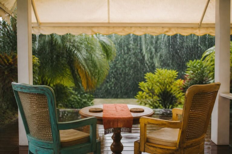 Two cane chairs sheltered beneath one canvas awning during tropical rain.
