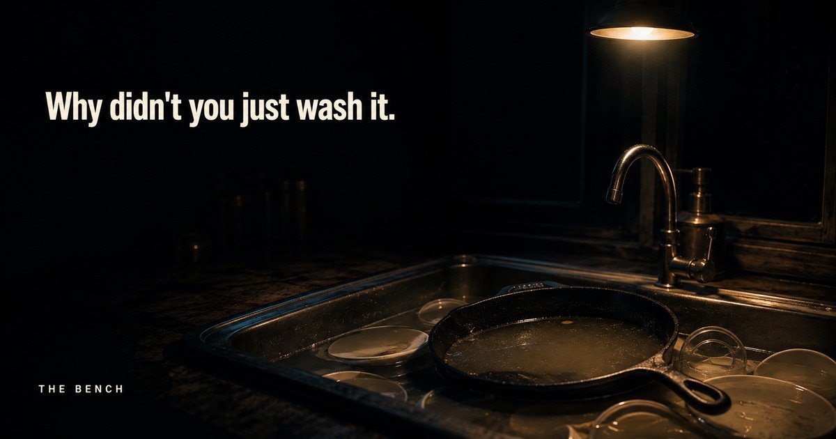 A heavy cast iron skillet sitting in a sink of cold water under a single kitchen light at night, with the words: Why didn't you just wash it.